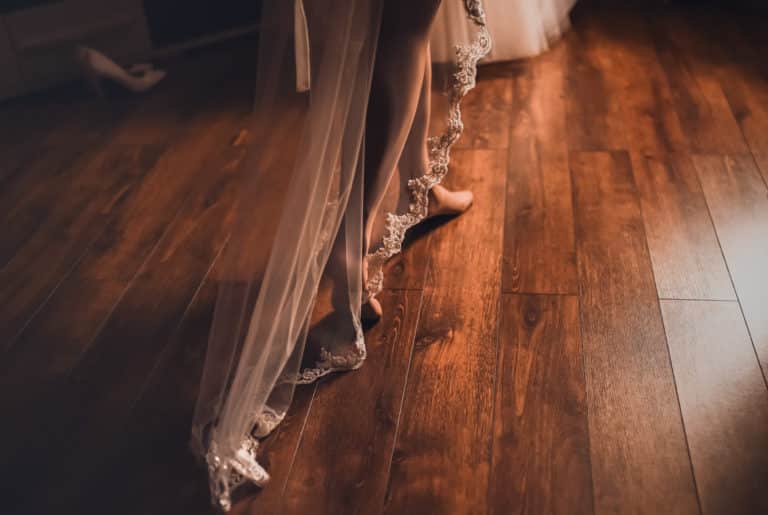 The bride's legs in white stockings walk along the brown wooden parquet floor